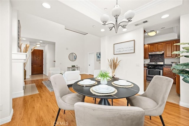 dining room featuring ornamental molding, a notable chandelier, light hardwood / wood-style floors, and a tray ceiling