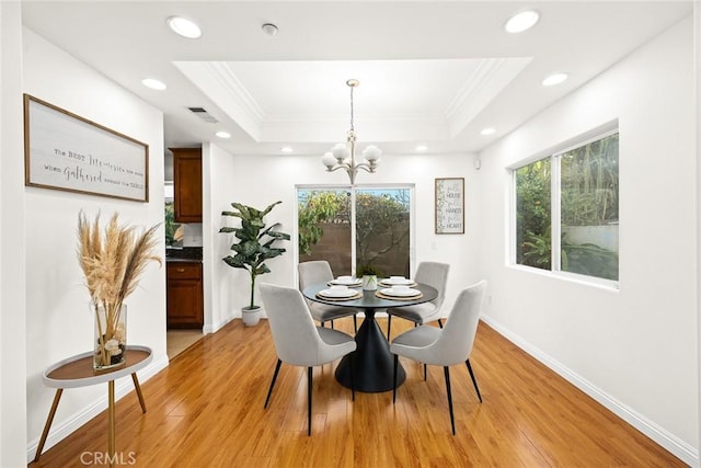 dining space featuring a raised ceiling, ornamental molding, and light wood-type flooring