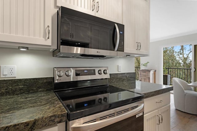 kitchen featuring hardwood / wood-style floors, appliances with stainless steel finishes, dark stone countertops, and white cabinets