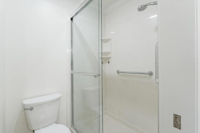 bathroom featuring crown molding, toilet, and a shower with shower door