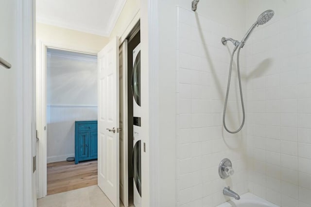 bathroom featuring tiled shower / bath, ornamental molding, and stacked washer and clothes dryer