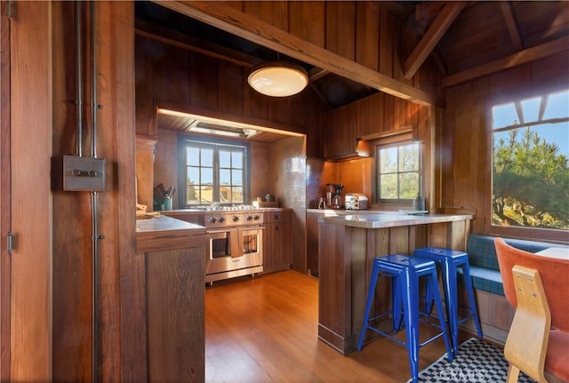 kitchen with a breakfast bar, wood walls, kitchen peninsula, high end stainless steel range oven, and light hardwood / wood-style floors