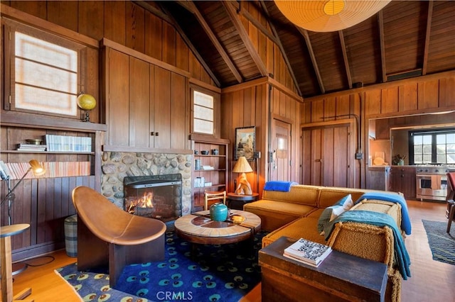 living room featuring beam ceiling, wooden walls, wooden ceiling, and a stone fireplace