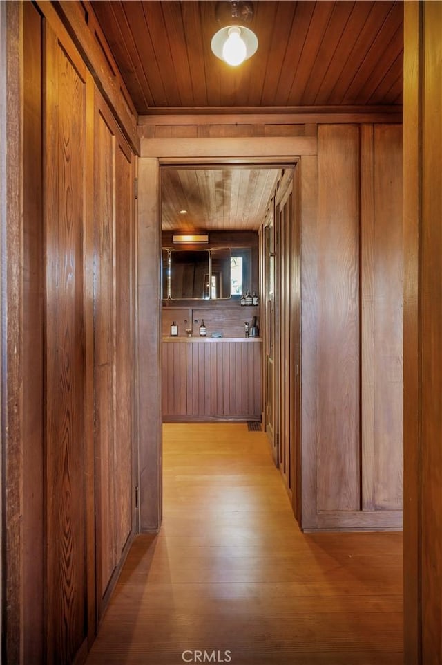 corridor with wood ceiling, wooden walls, and light hardwood / wood-style flooring