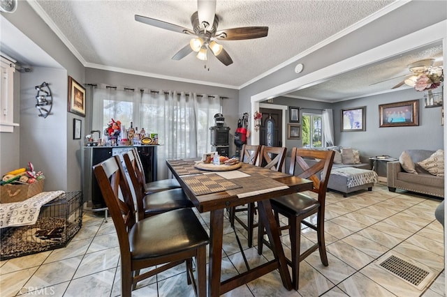 dining space with ornamental molding, bar, light tile patterned floors, ceiling fan, and a textured ceiling