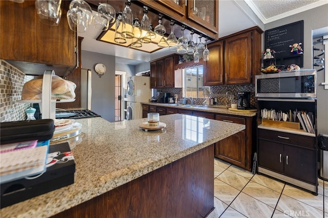 kitchen featuring stacked washer and dryer, dark brown cabinets, ornamental molding, light stone countertops, and decorative backsplash