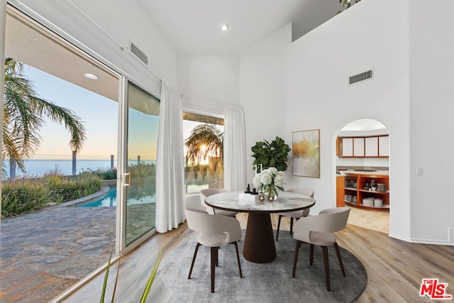 dining room featuring a towering ceiling, light hardwood / wood-style flooring, and a water view