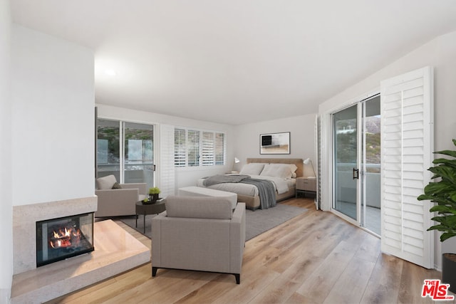 bedroom with access to outside, a premium fireplace, and light wood-type flooring