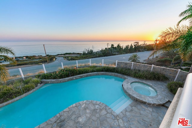 pool at dusk with an in ground hot tub and a water view