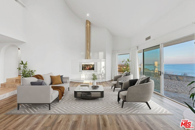 living room featuring a water view, high vaulted ceiling, a high end fireplace, and light hardwood / wood-style flooring