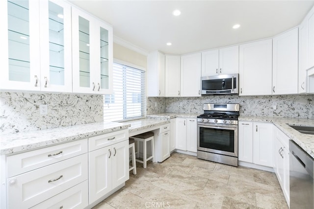 kitchen featuring tasteful backsplash, light stone counters, ornamental molding, stainless steel appliances, and white cabinets