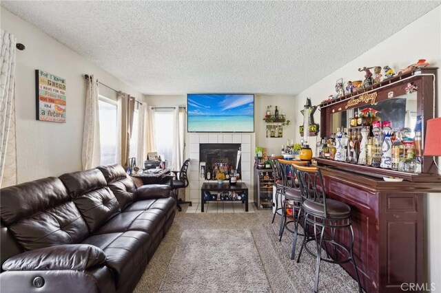 carpeted living room with a tile fireplace, a textured ceiling, and indoor bar