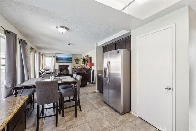 kitchen featuring light tile patterned flooring, a fireplace, stainless steel fridge, dark brown cabinets, and a textured ceiling