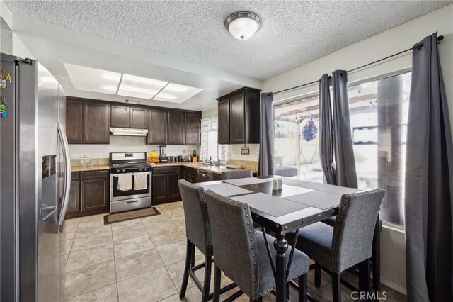 kitchen with light tile patterned floors, dark brown cabinets, a textured ceiling, and appliances with stainless steel finishes