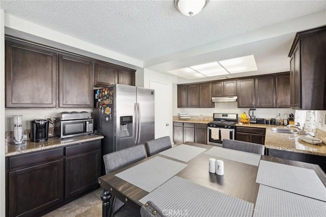 kitchen with appliances with stainless steel finishes, sink, dark brown cabinetry, light stone counters, and a textured ceiling