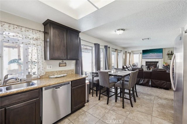 kitchen with sink, dark brown cabinets, a tile fireplace, and appliances with stainless steel finishes