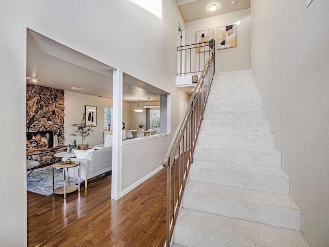 stairway with wood-type flooring and a stone fireplace