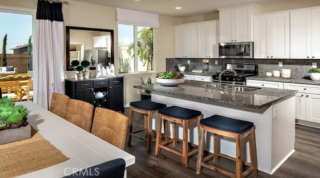 kitchen featuring sink, appliances with stainless steel finishes, white cabinetry, backsplash, and a kitchen island with sink