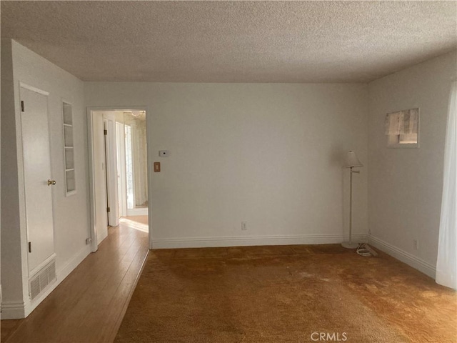 spare room featuring built in shelves, dark wood-type flooring, and a textured ceiling