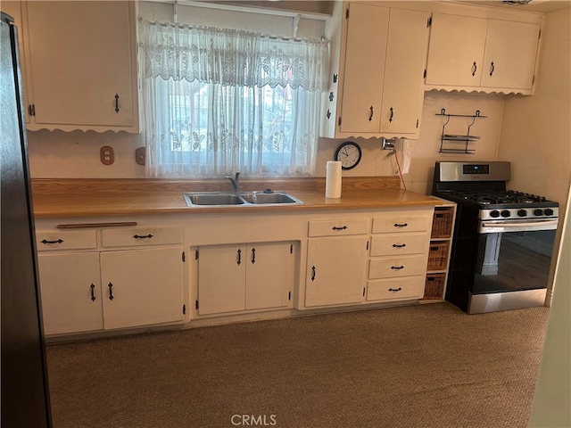 kitchen with white cabinetry, sink, stainless steel gas range oven, and black fridge