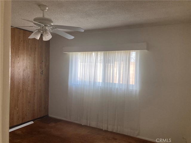 carpeted spare room featuring ceiling fan, wooden walls, and a textured ceiling