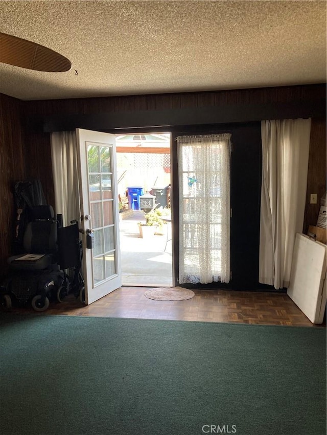 doorway featuring wooden walls, parquet floors, and a textured ceiling