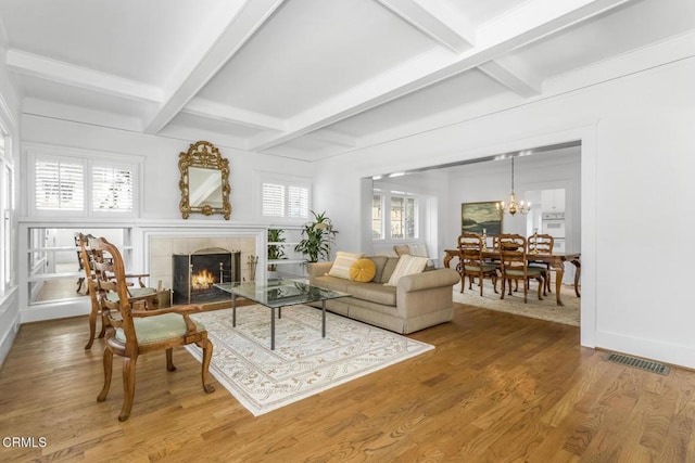 living room featuring hardwood / wood-style flooring, a chandelier, a tile fireplace, and beamed ceiling