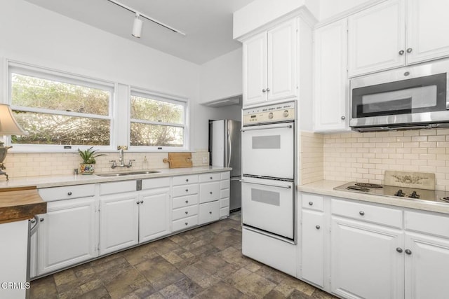 kitchen with sink, backsplash, white cabinets, and appliances with stainless steel finishes