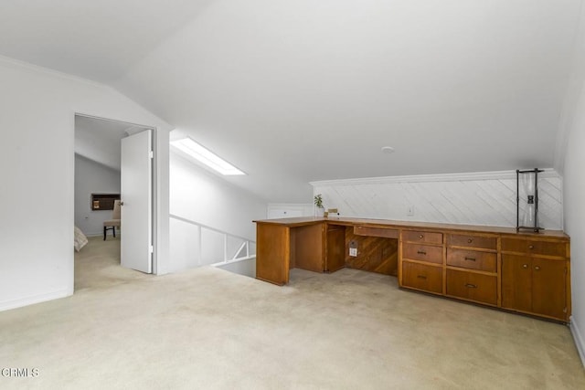 unfurnished office featuring vaulted ceiling with skylight, light colored carpet, and built in desk