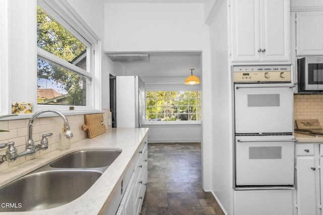 kitchen with pendant lighting, double oven, sink, white cabinets, and light stone counters