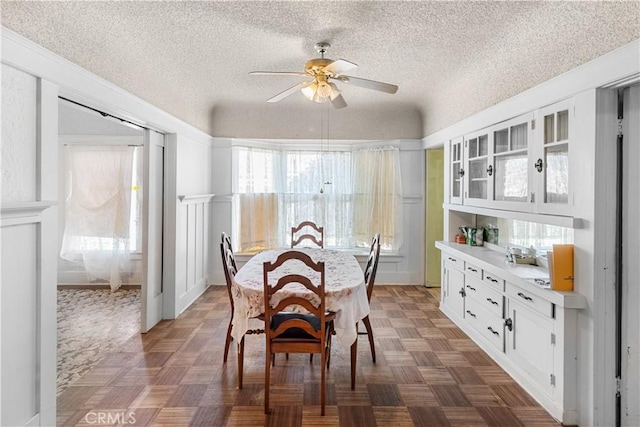 dining area featuring dark parquet flooring, a textured ceiling, and ceiling fan