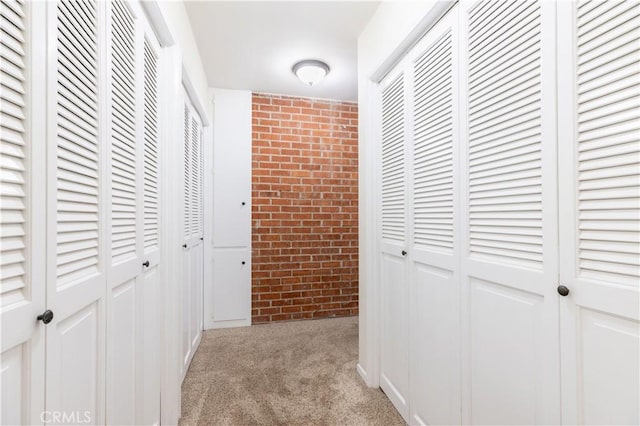 hall featuring carpet flooring and brick wall