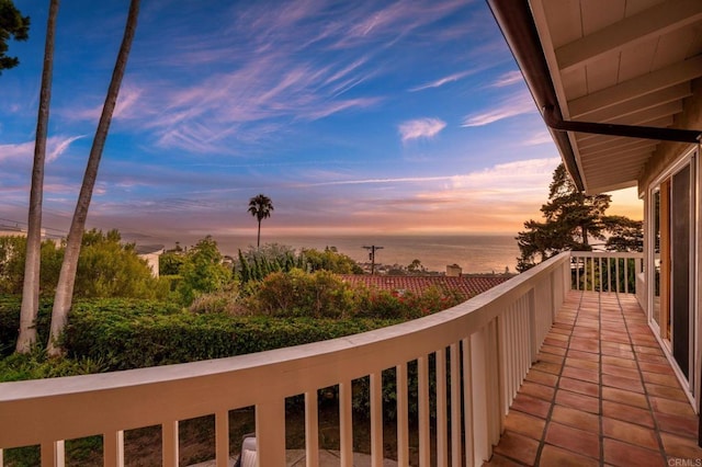 balcony at dusk featuring a water view