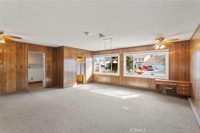 unfurnished living room featuring built in desk, light colored carpet, a textured ceiling, and wood walls