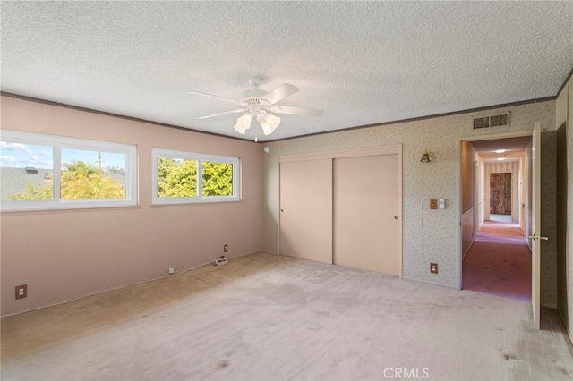 unfurnished bedroom with light carpet, crown molding, a closet, and a textured ceiling