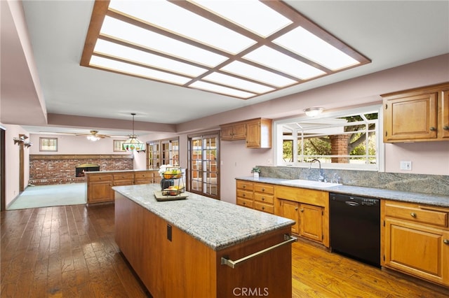 kitchen with sink, light stone counters, wood-type flooring, black dishwasher, and a kitchen island