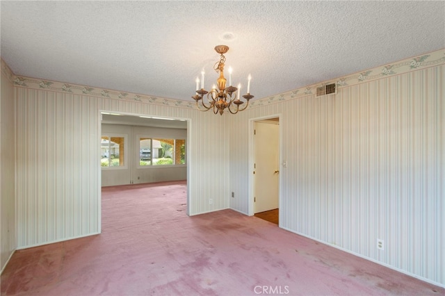 carpeted empty room featuring a notable chandelier and a textured ceiling