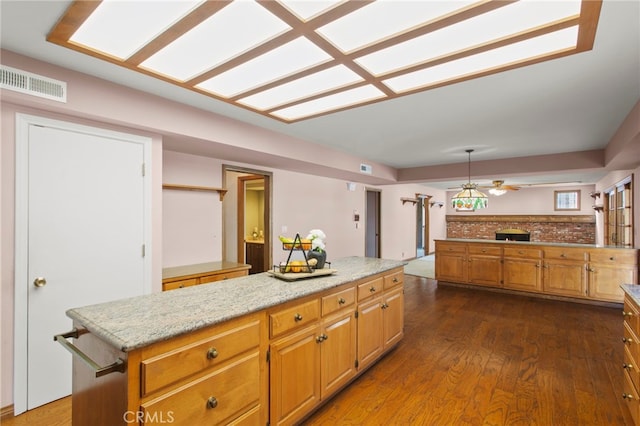 kitchen with dark hardwood / wood-style floors, pendant lighting, a center island, ceiling fan, and light stone countertops