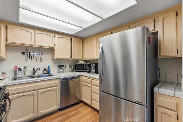 kitchen with appliances with stainless steel finishes, sink, tile counters, and light hardwood / wood-style flooring