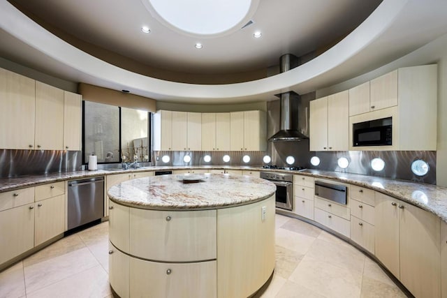 kitchen featuring wall chimney range hood, stainless steel appliances, a center island, cream cabinets, and light stone countertops