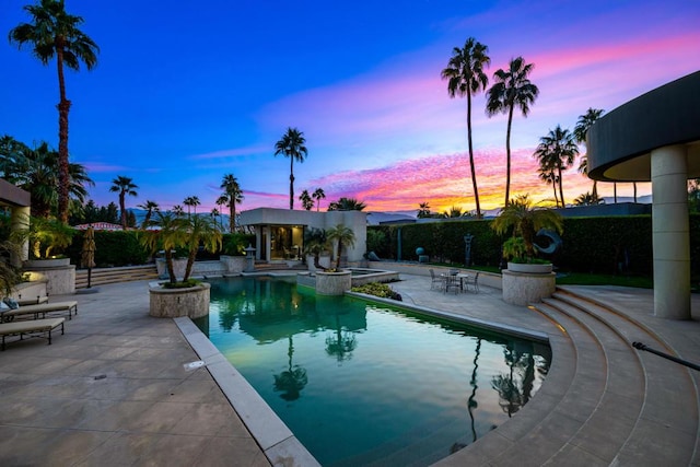 pool at dusk featuring a patio area and an in ground hot tub