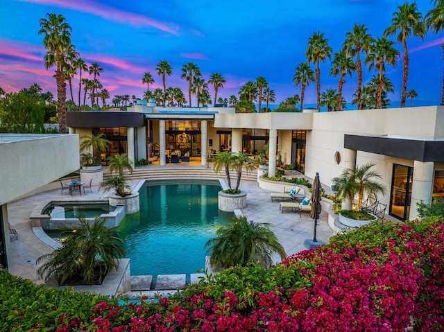 pool at dusk featuring an in ground hot tub and a patio