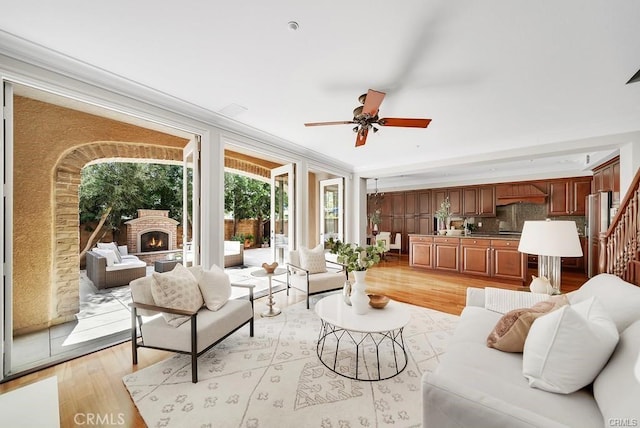 living room featuring a fireplace, ornamental molding, ceiling fan, and light wood-type flooring