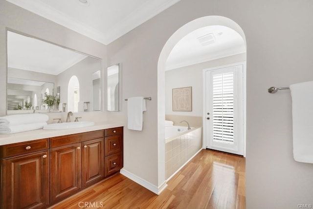 bathroom with tiled tub, vanity, hardwood / wood-style floors, and crown molding