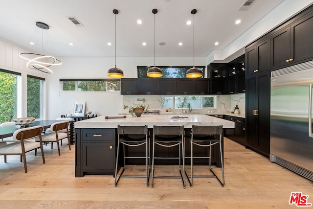 kitchen featuring stainless steel built in refrigerator, a large island, decorative light fixtures, and light hardwood / wood-style floors