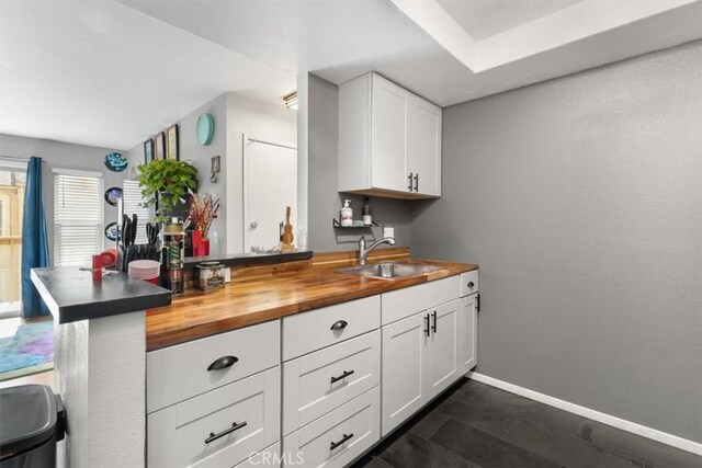 kitchen featuring butcher block counters, sink, kitchen peninsula, and white cabinets