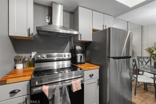 kitchen with wall chimney exhaust hood, stainless steel appliances, wooden counters, and white cabinets