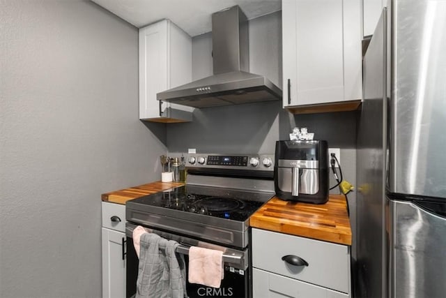 kitchen featuring white cabinetry, appliances with stainless steel finishes, butcher block counters, and wall chimney exhaust hood