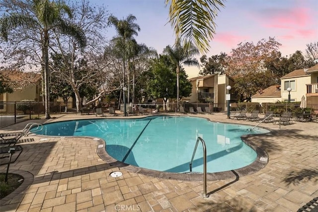 pool at dusk with a patio area, a community pool, and fence