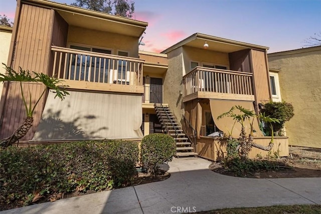 view of front of house featuring stucco siding, stairs, and a balcony